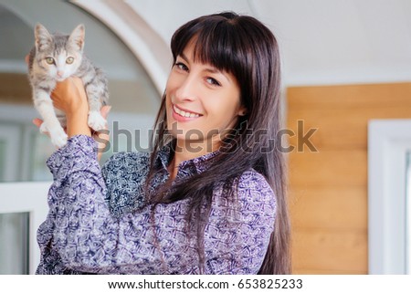 A beautiful girl with long black hair hugs a kitten. A model with clean skin. A gray kitten on his hands. Frontal to the animals.