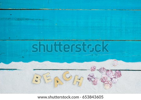 Collection of seashells and the word BEACH in sand border on antique rustic teal blue wood background; blank wooden beach sign with copy space