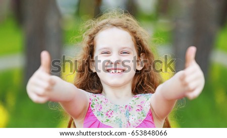 Laughing little girl  showing thumbs up.