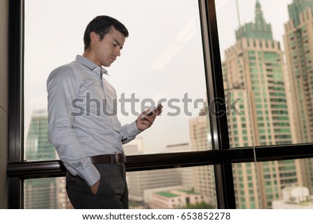Handsome businessman using on the phone in office with cityscape background.