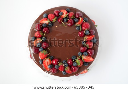 Birthday cake in chocolate with strawberries, blueberries and cherry on white background. Top view. Picture for a menu or a confectionery catalog.