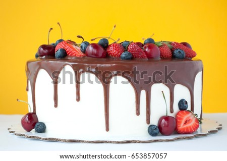 Birthday cake in chocolate with strawberries, blueberries and cherry on yellow background. Picture for a menu or a confectionery catalog.