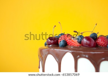 Birthday cake in chocolate with strawberries, blueberries and cherry on yellow background. Close-up. Picture for a menu or a confectionery catalog. Copy space for text.