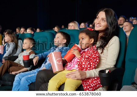 Young beautiful woman smiling holding her young daughter on the lap enjoying movie premiere at the cinema copyspace happiness living people leisure activity weekend togetherness concept.