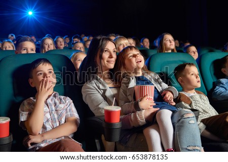 Low angle shot of people watching a movie at the cinema. Young woman and her daughter enjoying a film at the movie theatre motherhood parenting children kids entertaining happiness.