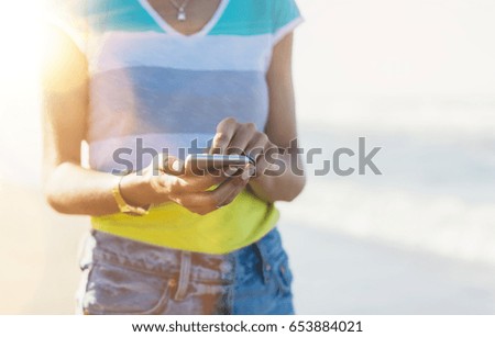 Hipster girl photograph on smart phone gadget in sand coastline, mock up of blank screen. Traveler hold and using in hand mobile on background seascape. Tourist look on blue sun ocean, lifestyle 