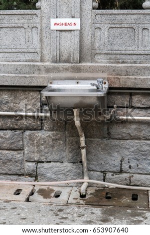 Steel sink hang on stone wall on street in city center. The empty public bathroom in Hong Kong.