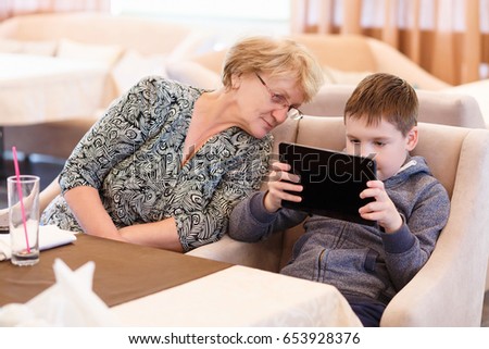Smiled grandmother with a grand child using a tablet while eating. Cartoons and games at mealtime problem