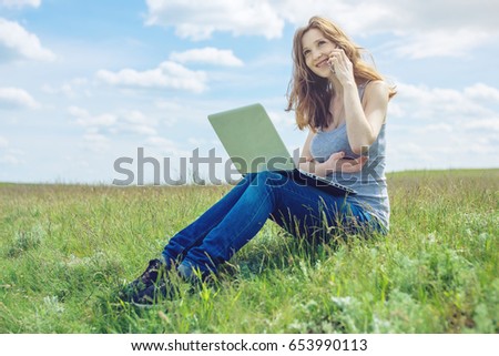 Woman sitting on a green meadow on the background of sky with clouds and working or studying with laptop wireless. The concept of nature and education