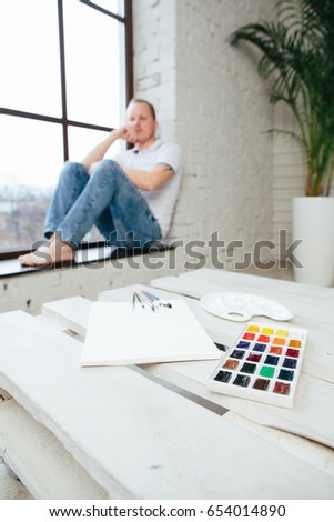 Creative crisis of a young man artist sitting near a sheet of paper and paints