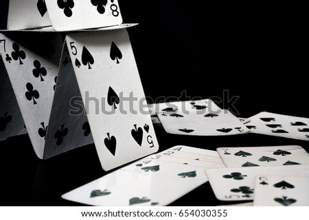 Playing cards forming a house of cards, and scattered white playing cards, black surface and background
