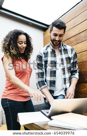 Two friends are studying while smiling and looking at laptop