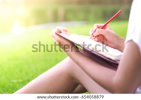 female hands with pencil writing on notebook in the park