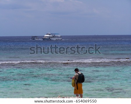 Photographer preparing his camera to take a picture of the turquoise ocean and the boat on it-stock photos