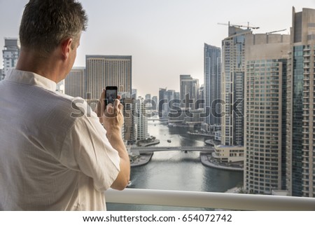 middle aged man taking picture of a marina view in Dubai with his mobile phone