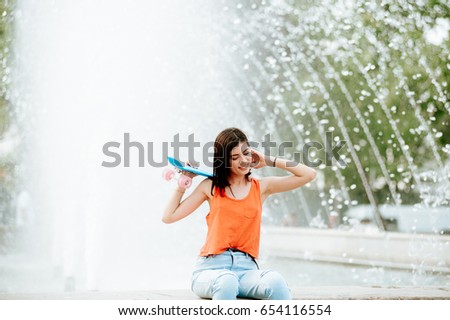 Beautiful attractive girl with penny board. Fashion pretty smiling beautiful girl having fun outside in city in hot summer day with her skateboard / penny board. Urban background
