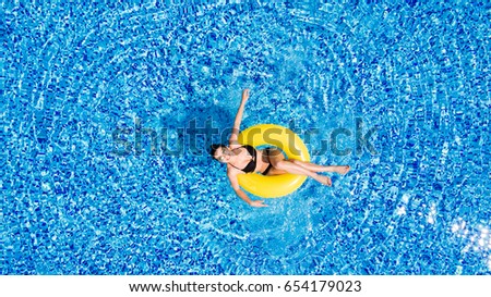Aerial view of young brunette woman swimming on the inflatable big yellow in the pool. Top view of slim lady relaxing on her holidays.