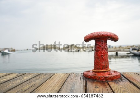 Red bollard with a mooring rope on the pier at the port and sea water in the background.  Sardinia, Italy.
