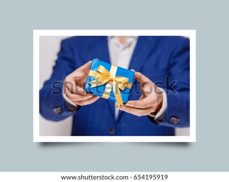 Male hands holding a gift box. Present wrapped with ribbon and bow. Christmas or birthday blue package. Man in suit and white shirt. Photo frame design with shadow.