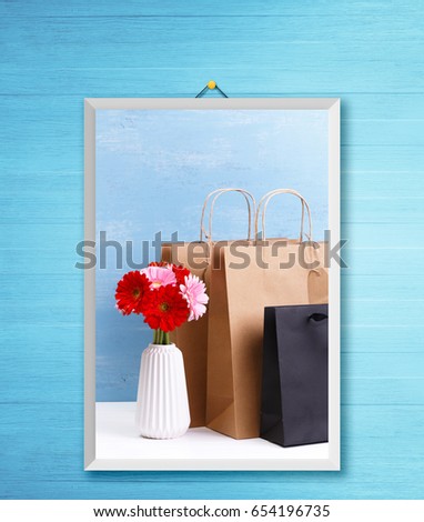 Mockup of blank shopping bags. Gerbera flowers in vase. Brown and black craft packages. Concept for sales or discounts. Blue wooden rustic board. Photo frame on wooden rustic wall.
