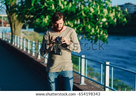 Happy casual hipster man making photo using retro camera outdoors in the park