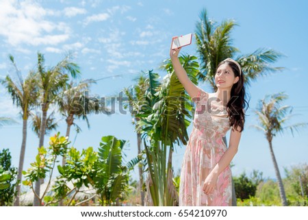 sweet woman going to tropical nation travel and using mobile smartphone taking selfie picture with coconut tree.