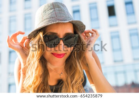 Sunny lifestyle close-up fashion portrait of young stylish hipster woman walking on the street, wearing trendy outfit and hat.