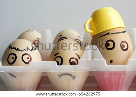 Eggs with a painted face in two rows. Transparent container. Photo for your design. One egg in a cup of coffee and yellow
