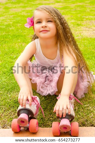 Little girl preschool beginner sitting in the grass with her roller skates, in a grass background