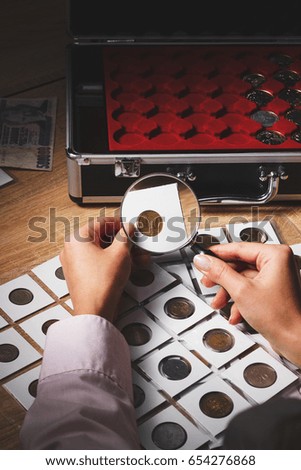 Old coin in the woman's hand through the magnifying glass, soft focus background