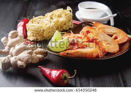 Asia culture. Fresh raw shrimp, noodles, chili pepper, ginger, soy sauce in a bowl on a wooden table. Eating seafood. Dark background