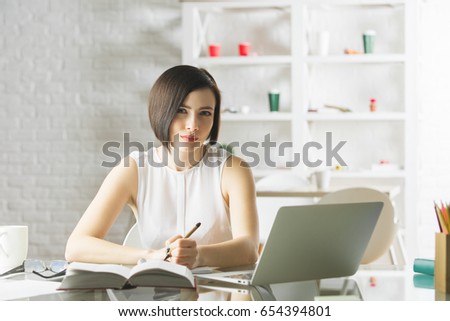 Portrait of beautiful young european female doing paperwork and using laptop in modern office. She is working on project