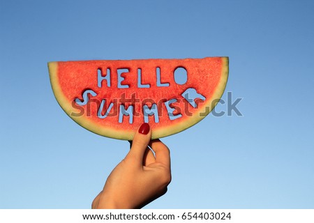 Watermelon slice  with text Hello Summer,  woman hands holding it against blue sky. Summertime concept. Royalty-Free Stock Photo #654403024