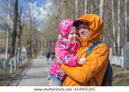 Dad is holding a daughter in his arms for a walk in the park. Spring day, family walk in nature, sunny.