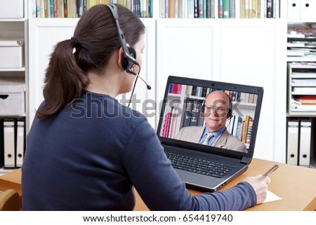Woman with pen and paper and a headset in front of her laptop making a video call with her friendly professor, text space Royalty-Free Stock Photo #654419740