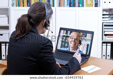 Female attorney-at-law with headset in front of a laptop on her desk giving online advice to an elderly client, legal helpline, copy space Royalty-Free Stock Photo #654419761