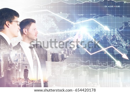 Two attractive businessmen drawing downward forex chart arrows on city background. Profit concept. Double exposure