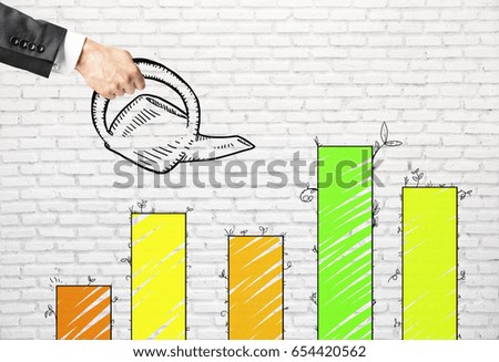 Side view of businessman's hand watering green business chart bars on brick background. Savings concept