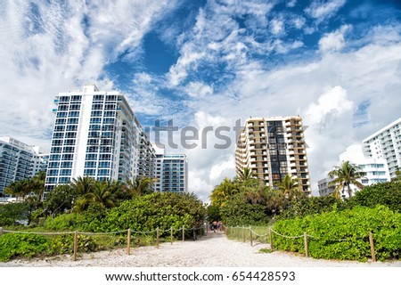 Miami beach or south beach. path way from tropical beach with green palm trees to high rise, apartment buildings or houses. City skyline with clouds on sunny day on blue sky. Idyllic summer vacation