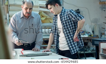 Senior male worker instructing young trainee how to construct a frame behind the desk in frame workshop