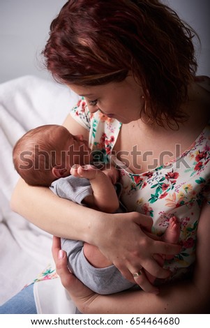  Young mom sitting with a newborn child . Happy family, mother kissing son or daughter , hugs . They are a happy family