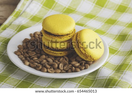 Yellow macarons on the plate with green coffee beans, soft focus background