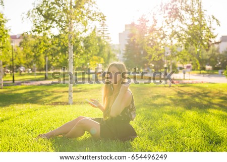 Girl listening to music streaming with headphones in summer on a meadow.