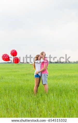 Man and woman on the field with red balloons. Happy couple on nature