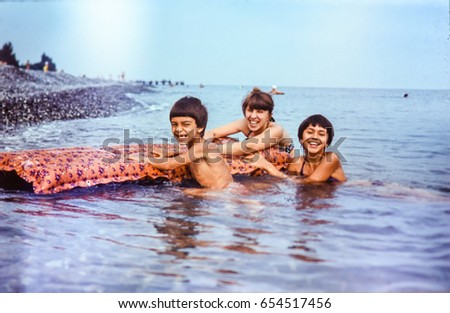 USSR, ABKHAZIA, LESELIDZE - CIRCA 1981: Vintage family photo of mother with children laughing in Black sea water at beach landscape