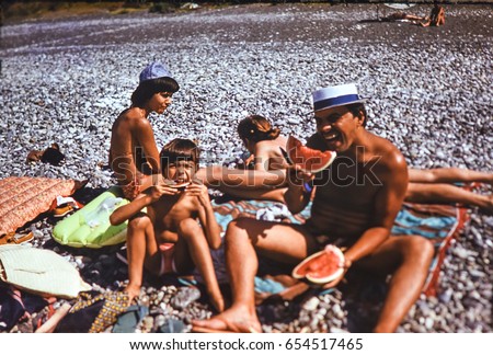 USSR, ABKHAZIA, LESELIDZE - CIRCA 1983: Vintage photo of happy family on beach eating ripe watermelon