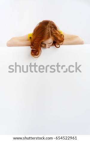 Redhead woman looking down at a blank sign bending forwards to look at the blank white copy space