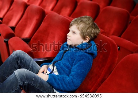 cute blond little kid boy eating popcorn at the cinema before the movie starts. Happy child having fun and waiting for the cartoon or film. Family day, leisure with children