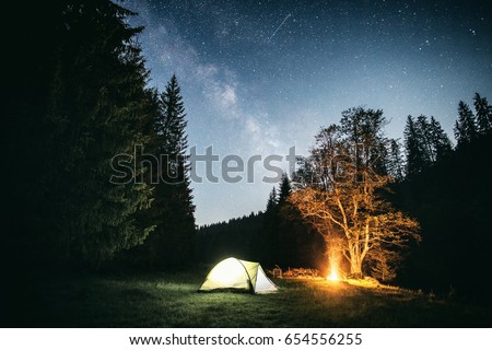 camping under the Milky Way with a campfire and glowing tent