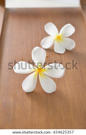 Two white plumeria (frangipani) flowers with wooden